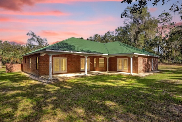 back house at dusk with a lawn, a patio area, and french doors