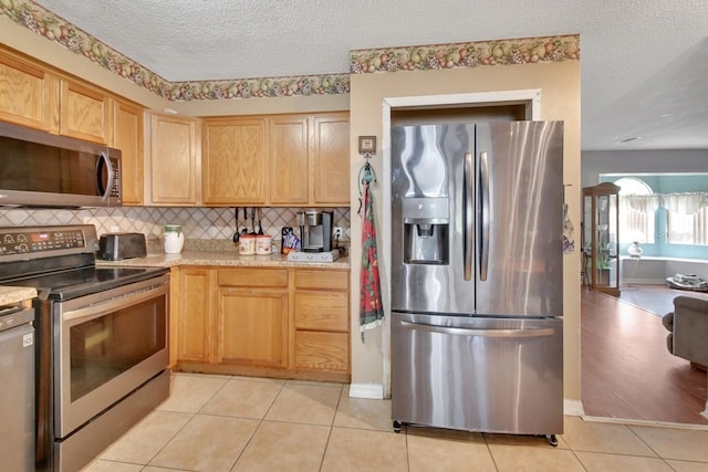 kitchen with backsplash, stainless steel appliances, a textured ceiling, and light tile patterned flooring