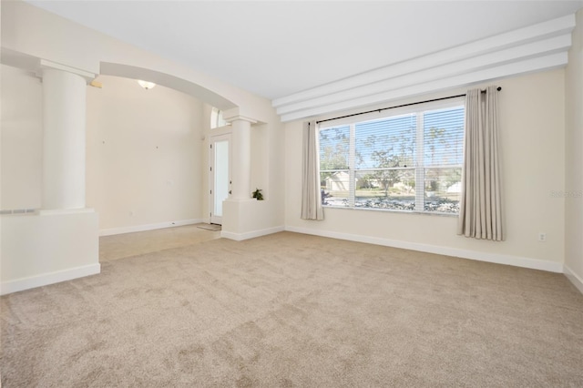 carpeted spare room featuring decorative columns, arched walkways, and baseboards