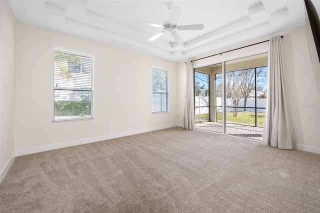 empty room with baseboards, a raised ceiling, carpet, and a ceiling fan