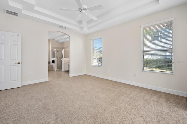 empty room featuring baseboards, visible vents, a tray ceiling, arched walkways, and light colored carpet