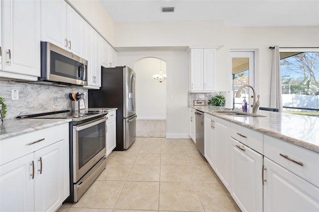 kitchen with light tile patterned floors, arched walkways, white cabinets, stainless steel appliances, and a sink