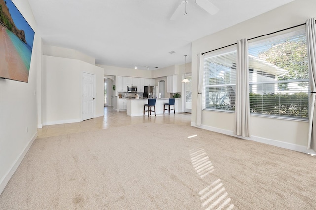 unfurnished living room featuring light tile patterned floors, light colored carpet, baseboards, and a ceiling fan