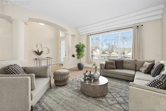 carpeted living room featuring baseboards, arched walkways, and ornate columns