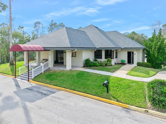 view of front of property with stucco siding, roof with shingles, and a front lawn