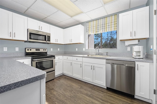 kitchen with a sink, appliances with stainless steel finishes, dark wood-style flooring, and white cabinetry