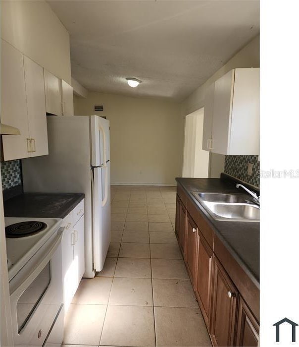 kitchen featuring sink, light tile patterned floors, white cabinets, white appliances, and backsplash