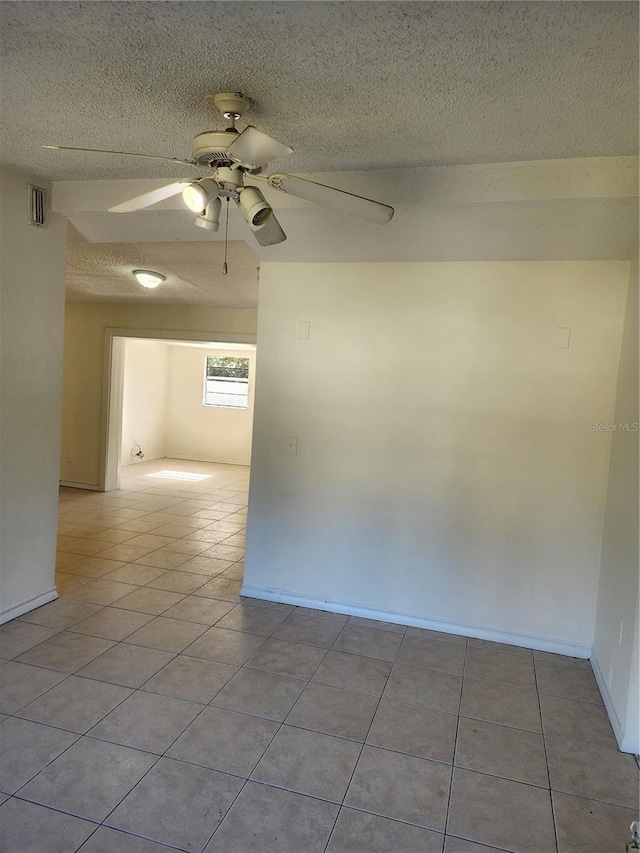 empty room featuring ceiling fan, light tile patterned floors, and a textured ceiling