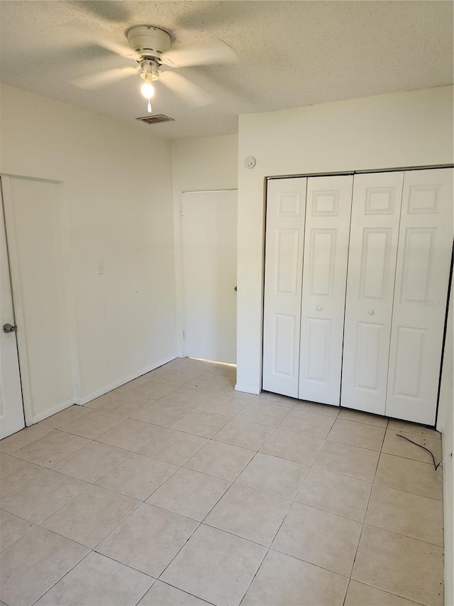 unfurnished bedroom featuring ceiling fan, light tile patterned floors, a textured ceiling, and a closet