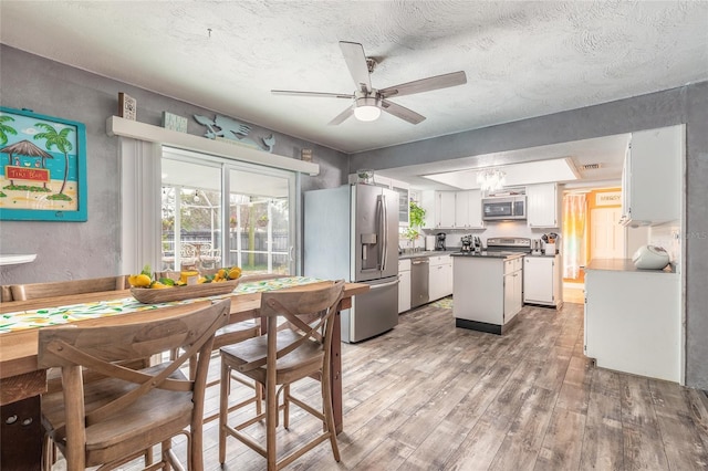 dining space featuring ceiling fan with notable chandelier, a textured ceiling, and wood-type flooring