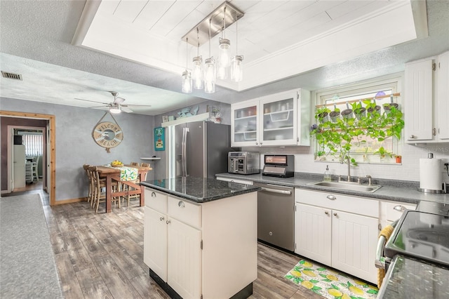 kitchen featuring hanging light fixtures, a raised ceiling, white cabinets, a kitchen island, and stainless steel appliances