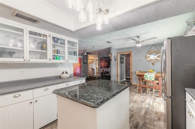 kitchen featuring wood-type flooring, white cabinetry, hanging light fixtures, a kitchen island, and stainless steel fridge