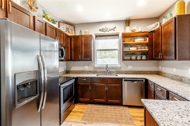 kitchen with sink, stainless steel appliances, light stone counters, and light hardwood / wood-style floors