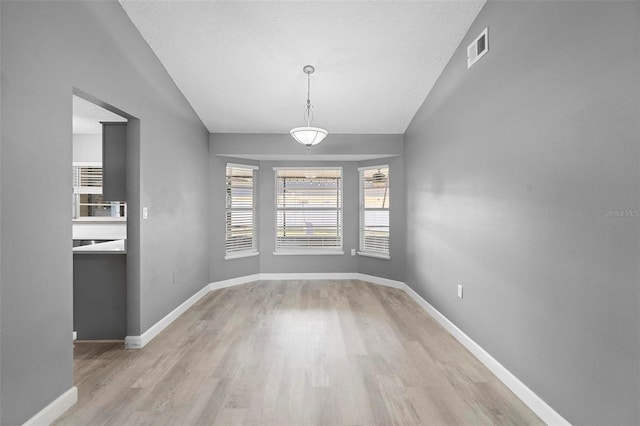 unfurnished dining area with lofted ceiling, light hardwood / wood-style floors, and a textured ceiling