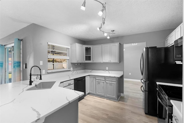 kitchen with sink, black appliances, light stone countertops, kitchen peninsula, and light wood-type flooring