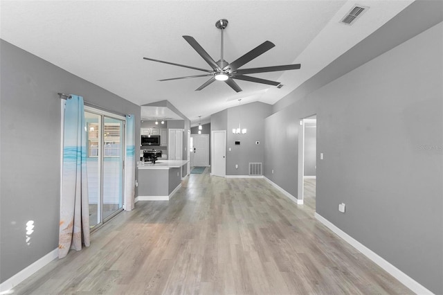 unfurnished living room featuring ceiling fan with notable chandelier, vaulted ceiling, and light wood-type flooring