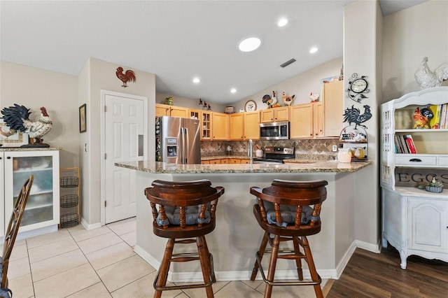 kitchen with light brown cabinetry, light stone countertops, kitchen peninsula, and stainless steel appliances