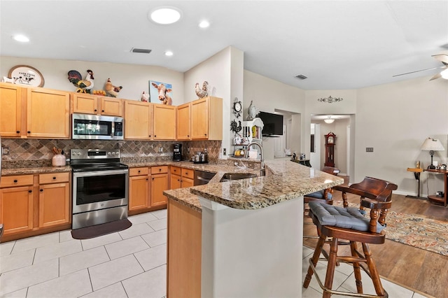 kitchen with light stone countertops, appliances with stainless steel finishes, a kitchen bar, sink, and kitchen peninsula