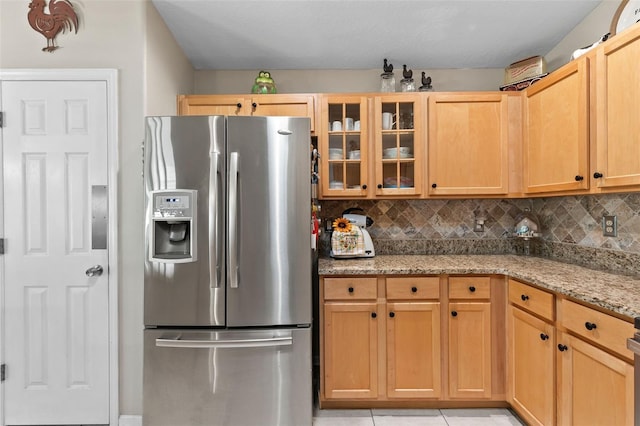 kitchen with light brown cabinetry, stainless steel fridge with ice dispenser, light tile patterned floors, decorative backsplash, and light stone counters