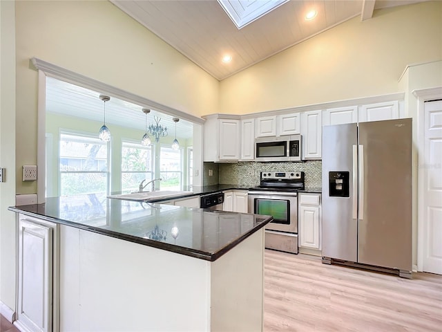 kitchen with appliances with stainless steel finishes, white cabinetry, tasteful backsplash, kitchen peninsula, and dark stone counters