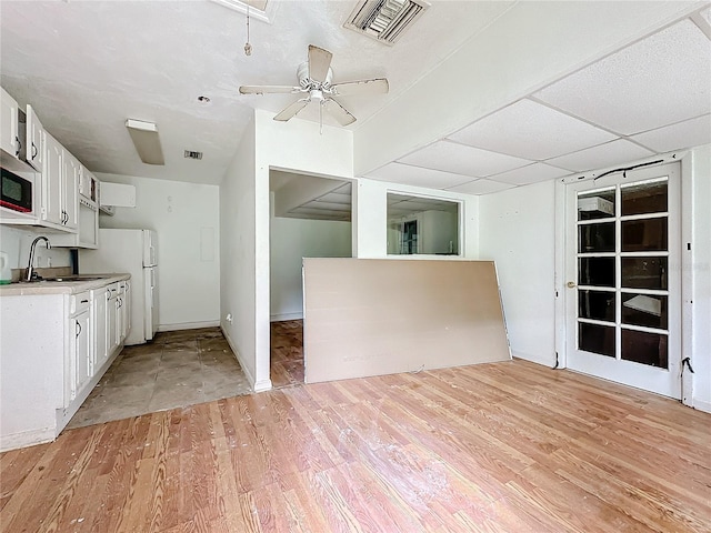 kitchen featuring sink, light hardwood / wood-style flooring, white cabinetry, white refrigerator, and a drop ceiling