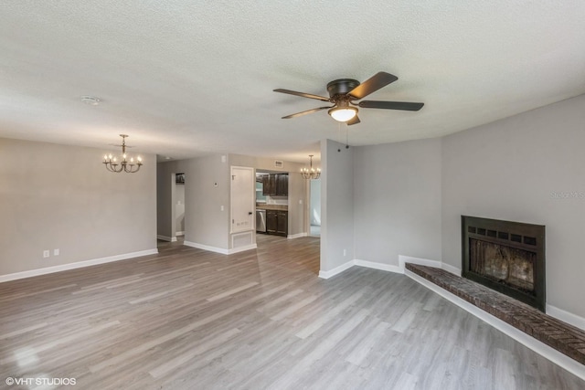 unfurnished living room featuring ceiling fan with notable chandelier, light wood-type flooring, and a textured ceiling