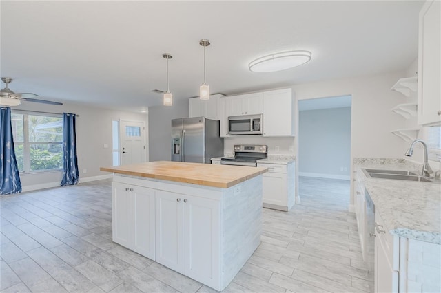 kitchen featuring appliances with stainless steel finishes, decorative light fixtures, sink, white cabinets, and a center island