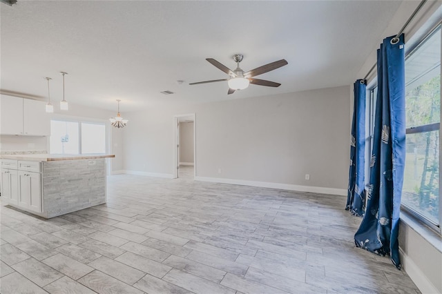 unfurnished living room with ceiling fan with notable chandelier and light wood-type flooring