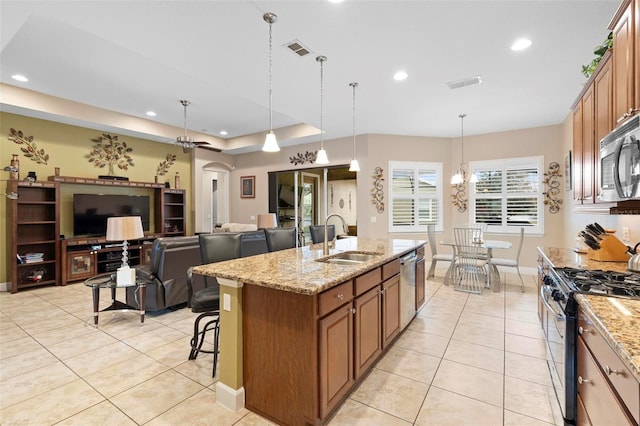 kitchen featuring appliances with stainless steel finishes, pendant lighting, an island with sink, sink, and light stone counters