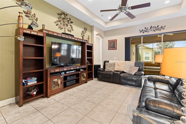 living room featuring ceiling fan, a tray ceiling, and light tile patterned floors