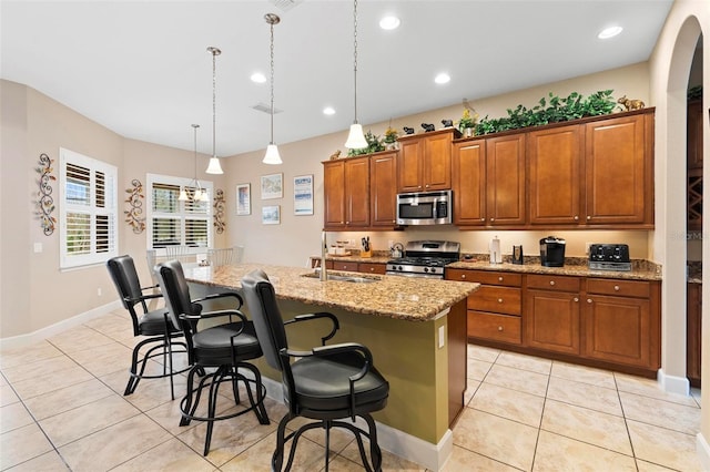 kitchen with sink, a breakfast bar area, appliances with stainless steel finishes, pendant lighting, and a kitchen island with sink