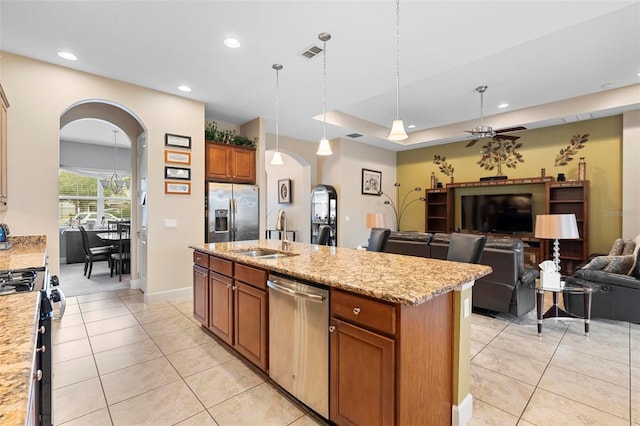 kitchen featuring sink, an island with sink, pendant lighting, stainless steel appliances, and light stone countertops