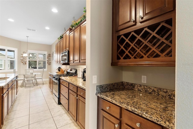 kitchen with appliances with stainless steel finishes, decorative light fixtures, light tile patterned floors, and stone counters