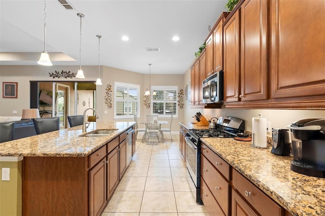 kitchen with pendant lighting, an island with sink, sink, light stone counters, and stainless steel appliances