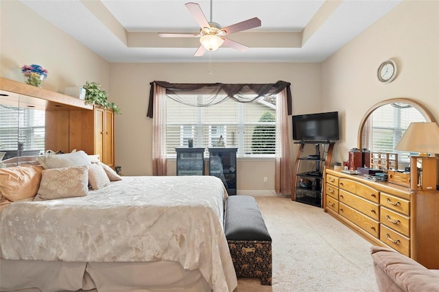 carpeted bedroom featuring a raised ceiling, ceiling fan, and multiple windows