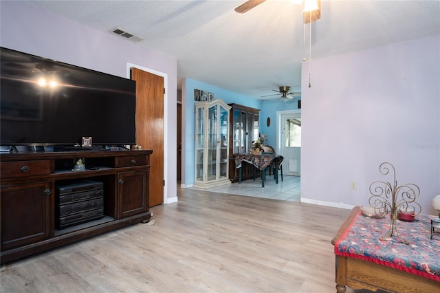 living room with ceiling fan, light hardwood / wood-style floors, and a textured ceiling