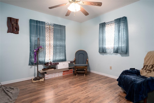 living area with ceiling fan, wood-type flooring, and a textured ceiling