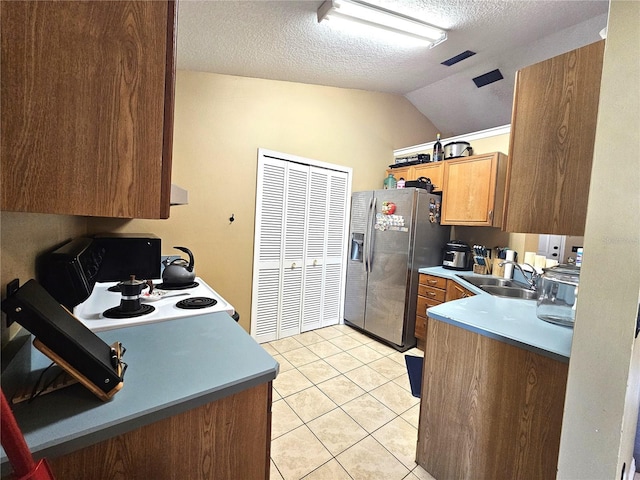 kitchen with light tile patterned flooring, sink, vaulted ceiling, a textured ceiling, and stainless steel fridge