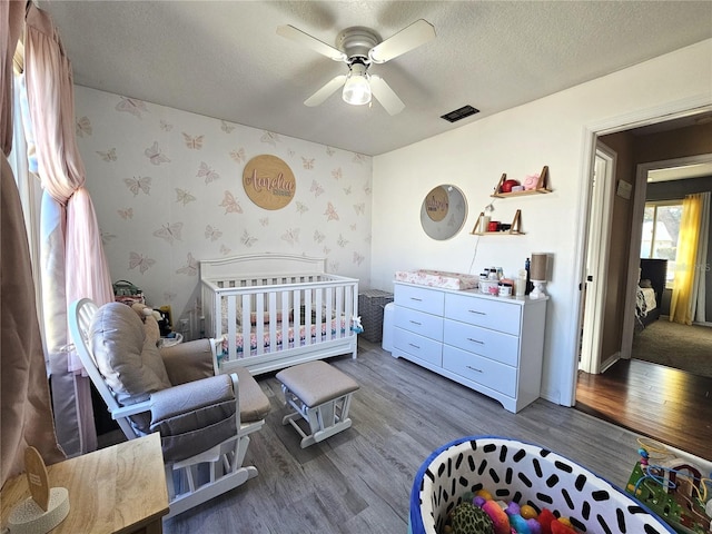 bedroom with hardwood / wood-style flooring, a crib, a textured ceiling, and ceiling fan