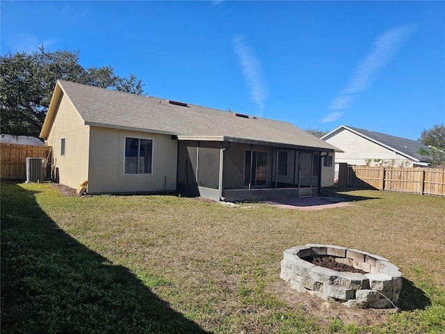 back of house with central AC, an outdoor fire pit, a sunroom, and a lawn