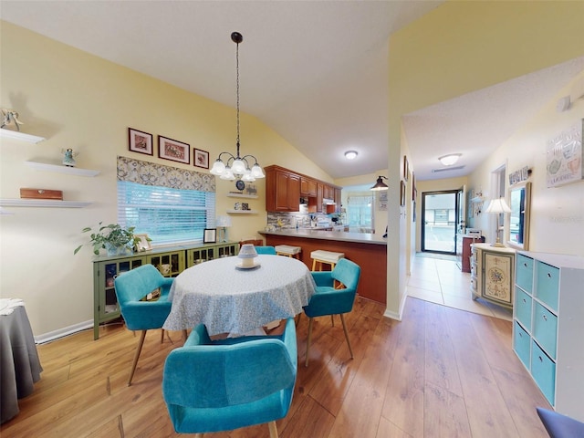 dining room featuring a notable chandelier, vaulted ceiling, and light wood-type flooring