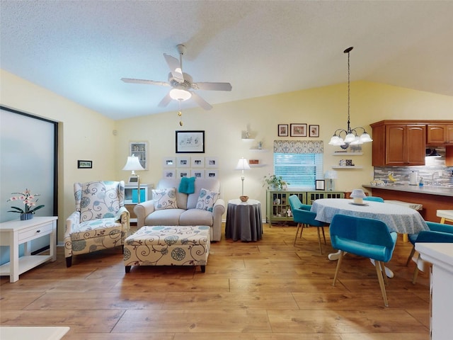 living room featuring vaulted ceiling, ceiling fan with notable chandelier, a textured ceiling, and light wood-type flooring