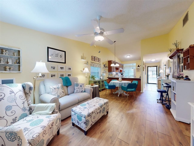 living room featuring lofted ceiling, ceiling fan with notable chandelier, and light wood-type flooring