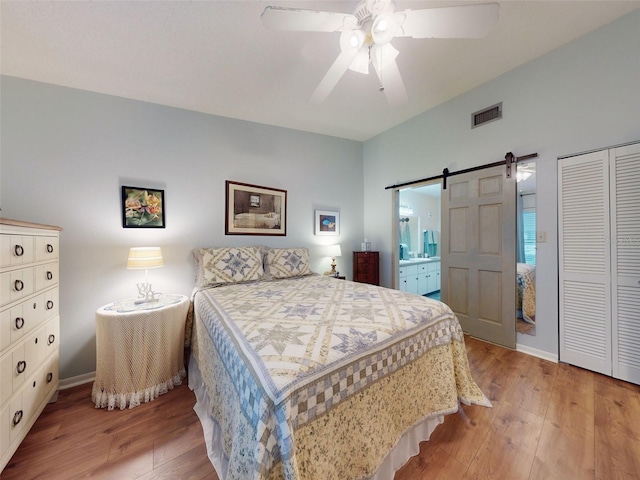 bedroom with ensuite bath, ceiling fan, a barn door, a closet, and light wood-type flooring