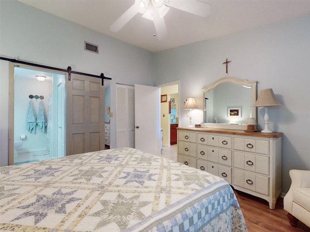 bedroom with connected bathroom, light wood-type flooring, a closet, ceiling fan, and a barn door