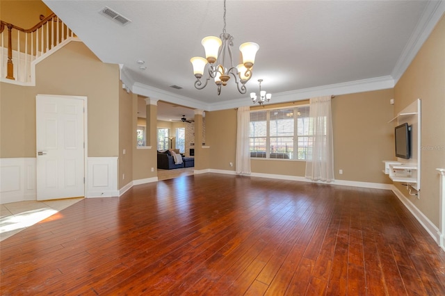 unfurnished living room with decorative columns, visible vents, ornamental molding, hardwood / wood-style floors, and ceiling fan with notable chandelier