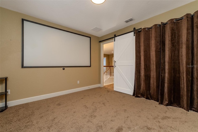 carpeted cinema room with a barn door, visible vents, and baseboards