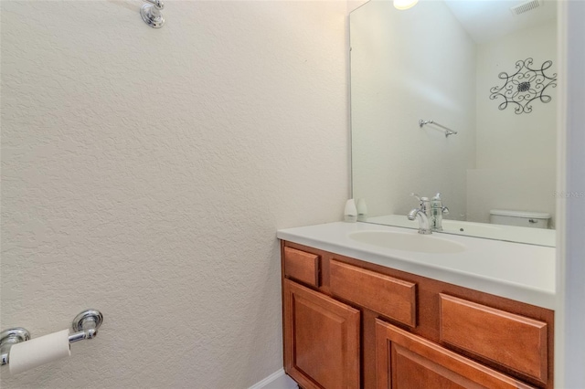 half bath with visible vents, a textured wall, toilet, and vanity