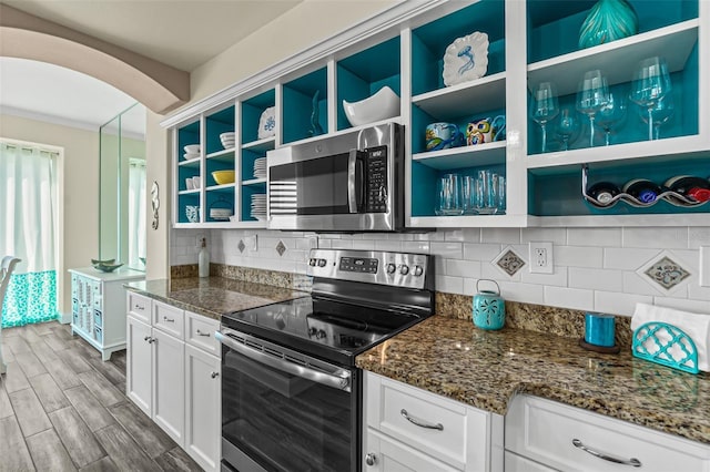 kitchen with appliances with stainless steel finishes, dark stone countertops, white cabinets, and backsplash