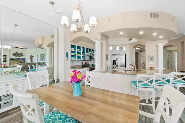 dining room with ceiling fan with notable chandelier, wood-type flooring, sink, and ornate columns